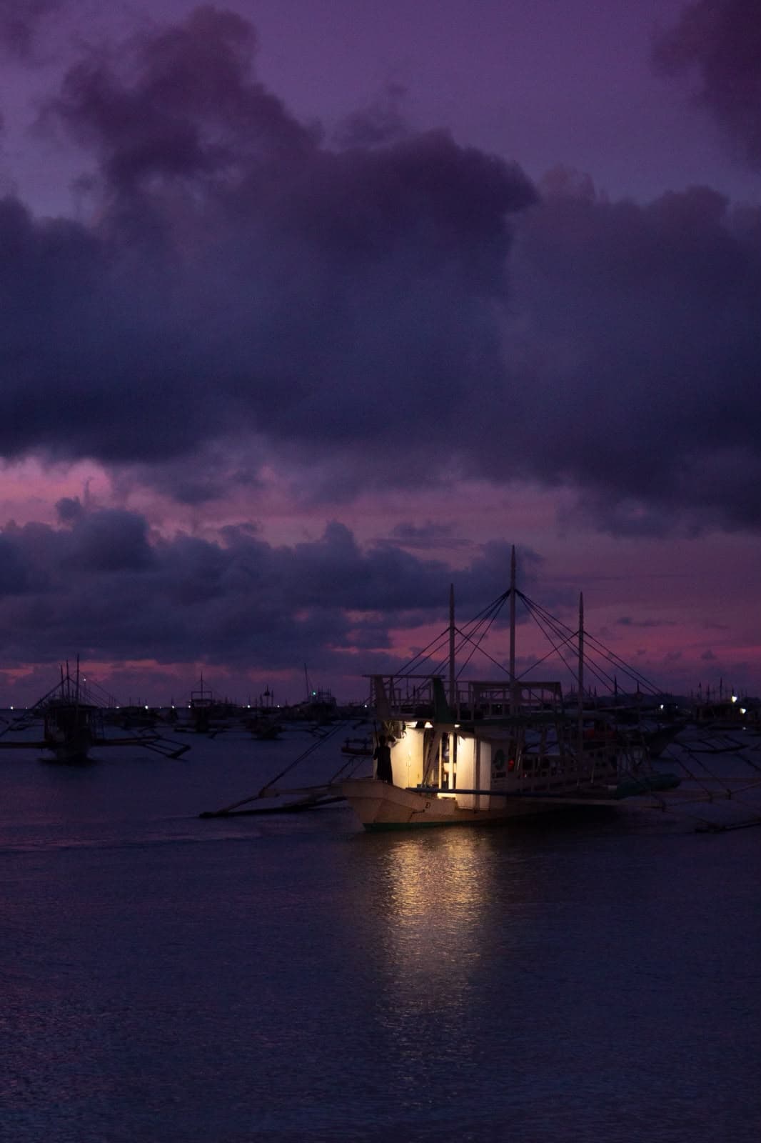 A lit boat at dusk, harbour lights