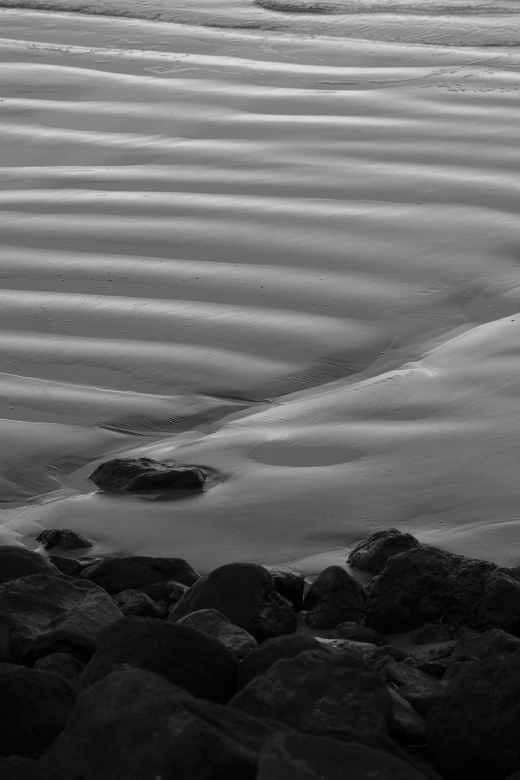 Rippled sand and dark rocks, in black and white